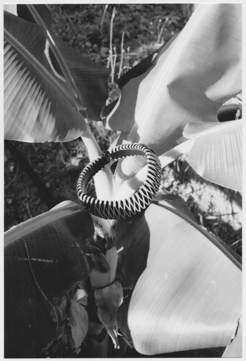 Artistic black and white image showcases a decorative woven bracelet on a large leaf, creating a striking contrast in texture and form.