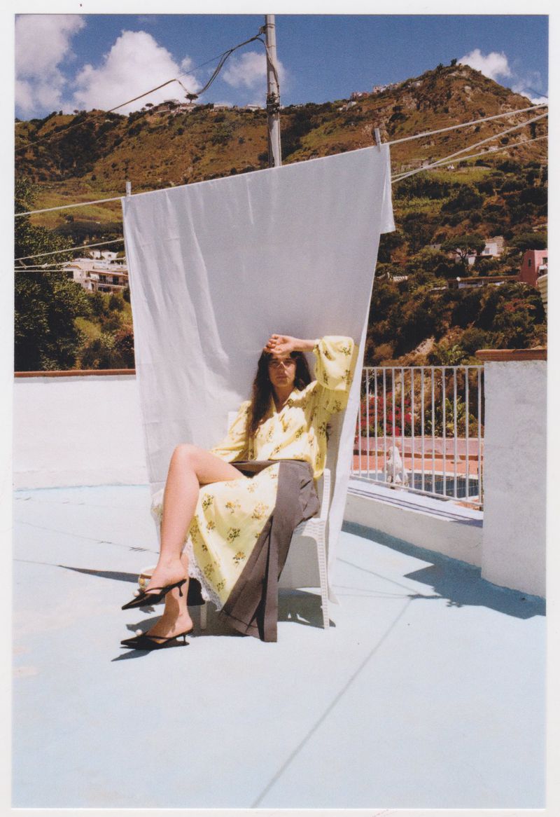 Matilde Giannetti seated in a chair before a hanging white sheet on a sunny rooftop terrace overlooking hills.