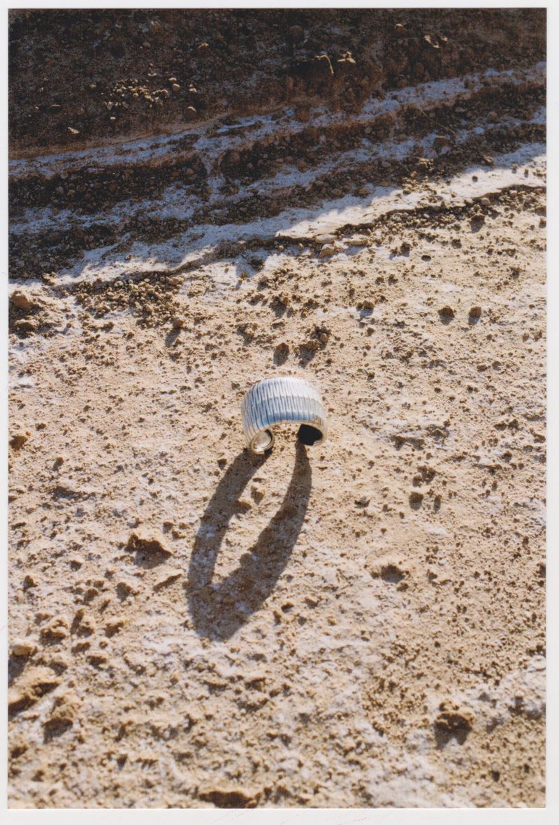 Silver metal cuff bracelet on a tan desert surface with textured land formation background, casting a distinct shadow in sunlight.