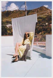 Matilde Giannetti seated in a chair before a hanging white sheet on a sunny rooftop terrace overlooking hills.