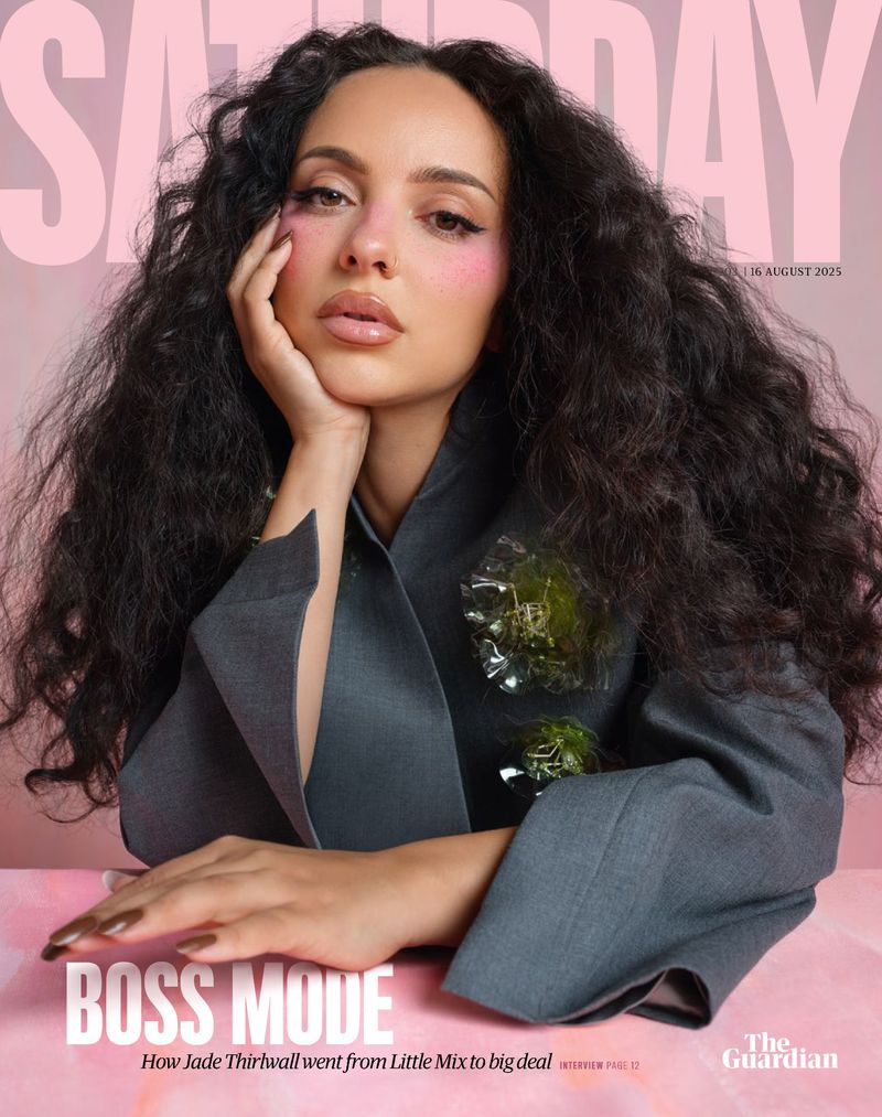 Portrait of Jade Thirlwall on magazine cover, wearing gray suit, with long curly hair and pink blush. The background is pink.