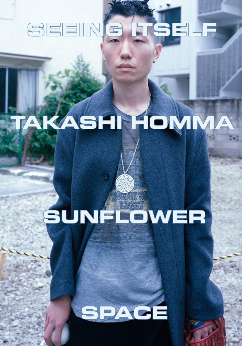 Portrait of an Asian male in a blue coat, standing outdoors in front of building. He is holding a baseball and mitt.