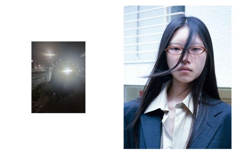 Portrait of an Asian woman with long dark hair, wearing a blue blazer and glasses, with a blurred photo in the background.