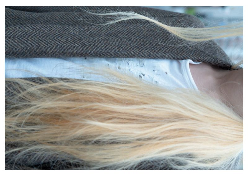 Close-up shot of an adult female with long blonde hair wearing a white shirt and brown tweed jacket in an indoor setting.