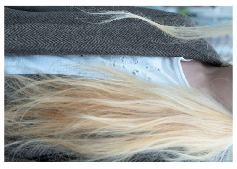 Close-up shot of an adult female with long blonde hair wearing a white shirt and brown tweed jacket in an indoor setting.