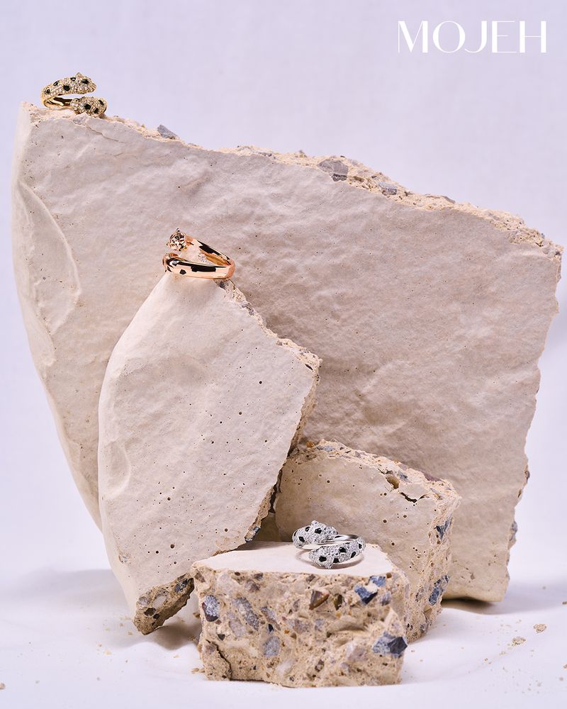 Jewelry product shot features three gold rings with black and white stones, artfully arranged on pieces of white stone on a white background.