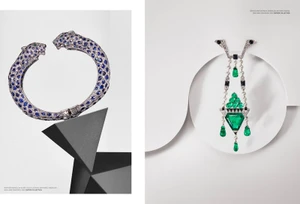 Cartier sapphire panther bangle and emerald pendant brooch displayed on minimalist geometric props against a white studio background.