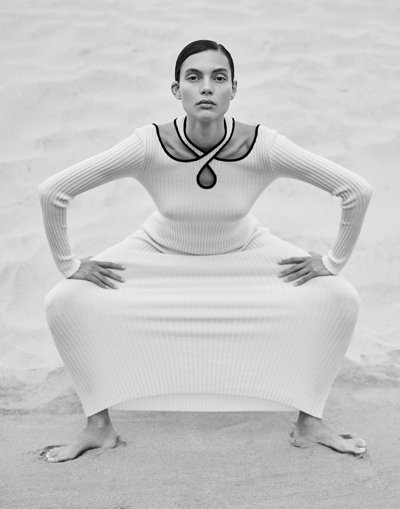 Charlee Fraser crouching in a long white ribbed dress on sand for Harper's Bazaar Australia, photographed by Justin Woo