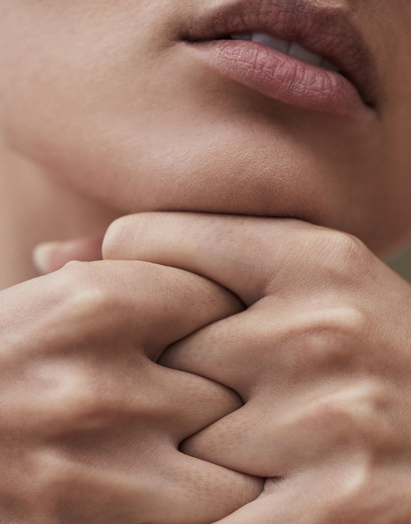 Close-up shot of a person's face and hands, featuring clean, smooth skin and a neutral expression, in a soft, diffused light.