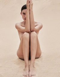 Charlee Fraser seated on sand dunes with raised arms covering her face for Harper's Bazaar Australia