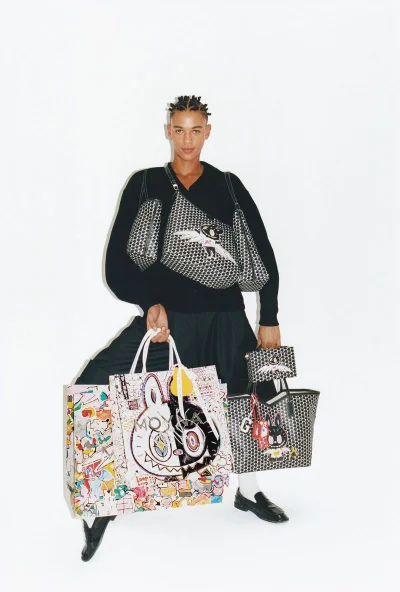 Guillaume Diop in black knitwear holding several printed Moynat x Kasing Lung tote bags against a seamless white background.
