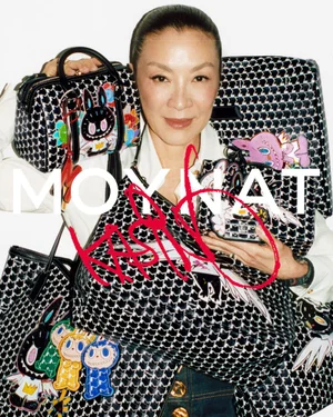 Michelle Yeoh smiling while surrounded by Moynat Kasing Lung patterned handbags and luggage against a white background