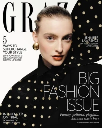Berit Heitmann poses for a magazine cover wearing a black polka-dot top and a large gold earring against a white background.