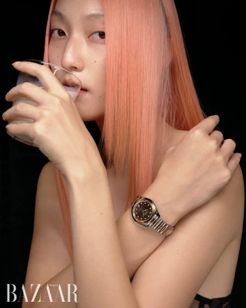 Close-up studio shot of an adult woman with pink hair drinking milk. She wears a wrist watch against a dark background.
