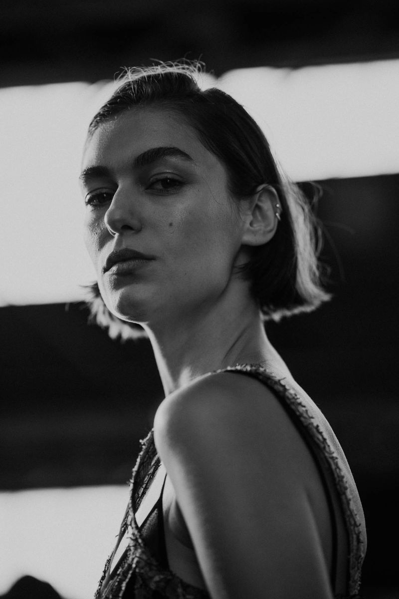 Monochrome portrait of a young woman with short dark hair, looking directly at the camera in an indoor setting with soft light.