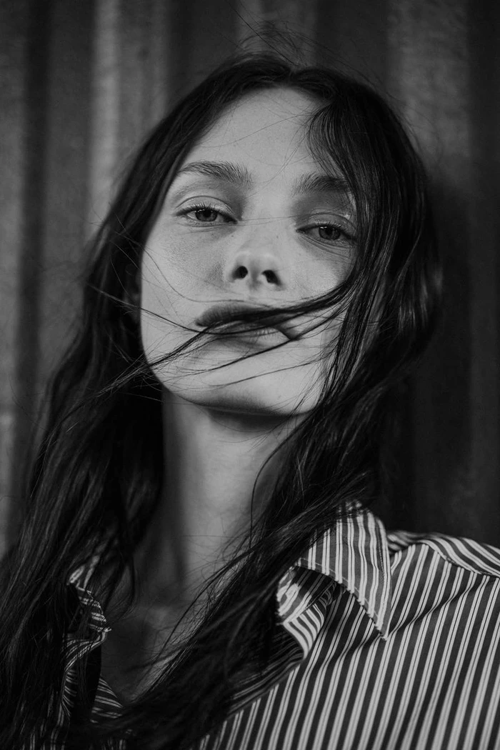 Close-up monochrome portrait of a model with dark hair wearing a striped shirt against a textured background.