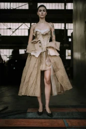 Model wearing a structured beige strapless dress standing in an industrial warehouse interior for Jason Wu SS26 show backstage