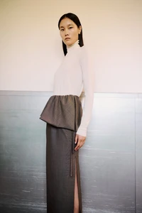 Model Canlan Wang in a white high-neck top and charcoal peplum maxi skirt with side slit for Adam Lippes Spring 2026.