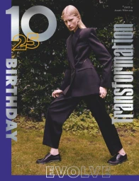 Model posing in a tailored black suit and black dress shoes with a wide stance on grass for the cover of 10 Magazine.