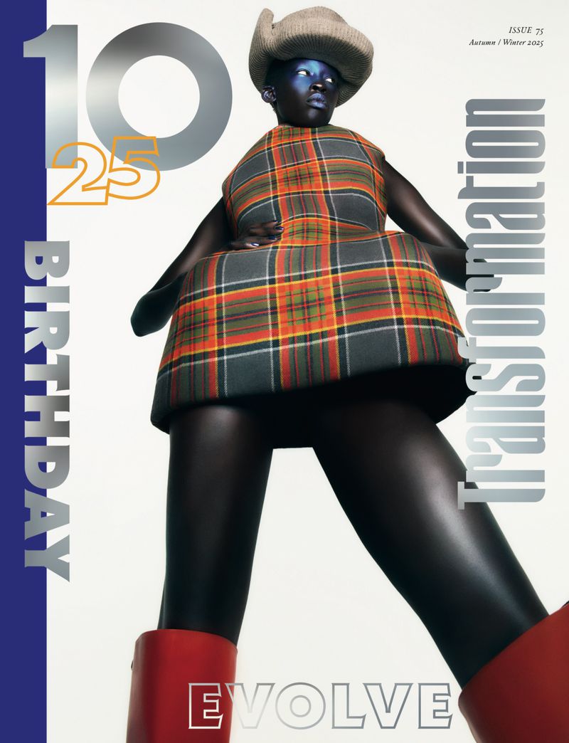 Fashion editorial shot of a model wearing a plaid dress, hat, and red boots, posing against a gradient grey-to-white background.