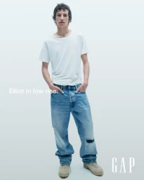 Elliot Belot in a white t-shirt and distressed low rise blue jeans posing against a clean seamless background for Gap.