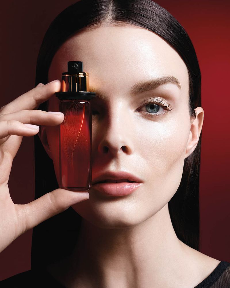 Close-up of a woman holding a perfume bottle, presenting the beauty product with a vibrant red background and diffused light.
