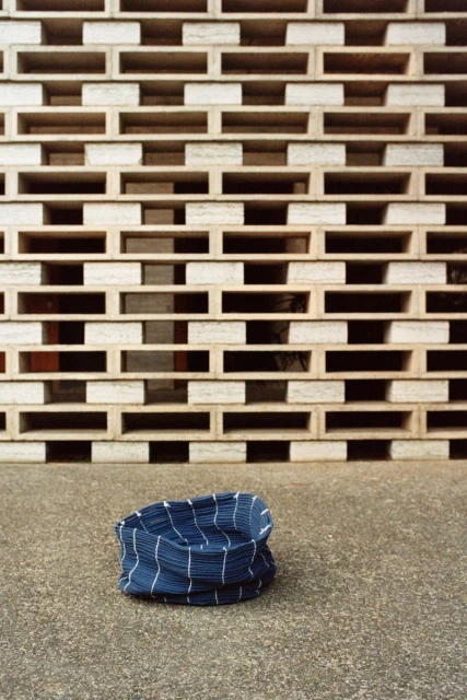 Blue and white striped fabric form on concrete against wall of square cubbies. Minimalist textile product still life image.