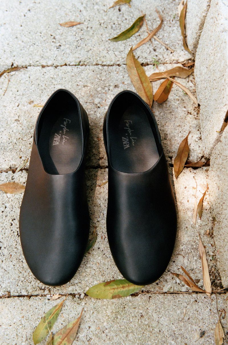 Overhead shot of pair of black leather slip-on shoes on a stone surface with fallen leaves, showcasing fashion footwear.