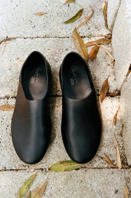 Overhead shot of pair of black leather slip-on shoes on a stone surface with fallen leaves, showcasing fashion footwear.