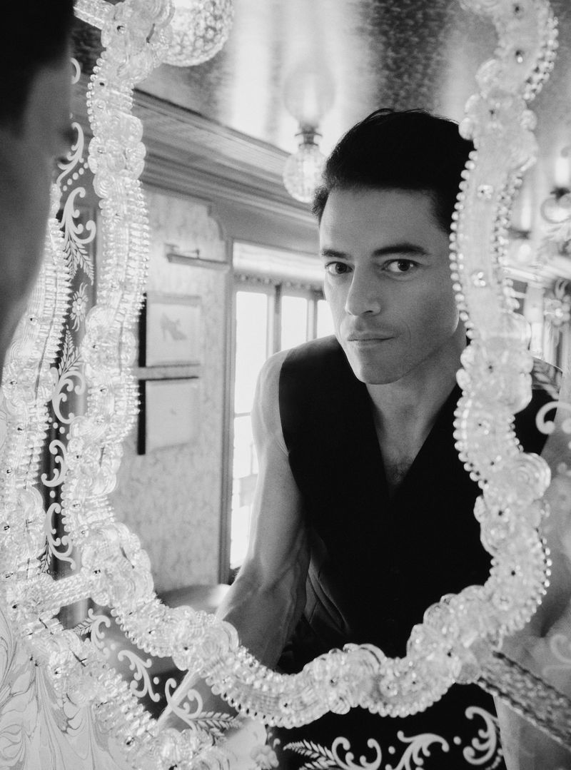 Black and white portrait of a male reflected in a decorative mirror inside of an ornate building, showcasing architectural details.