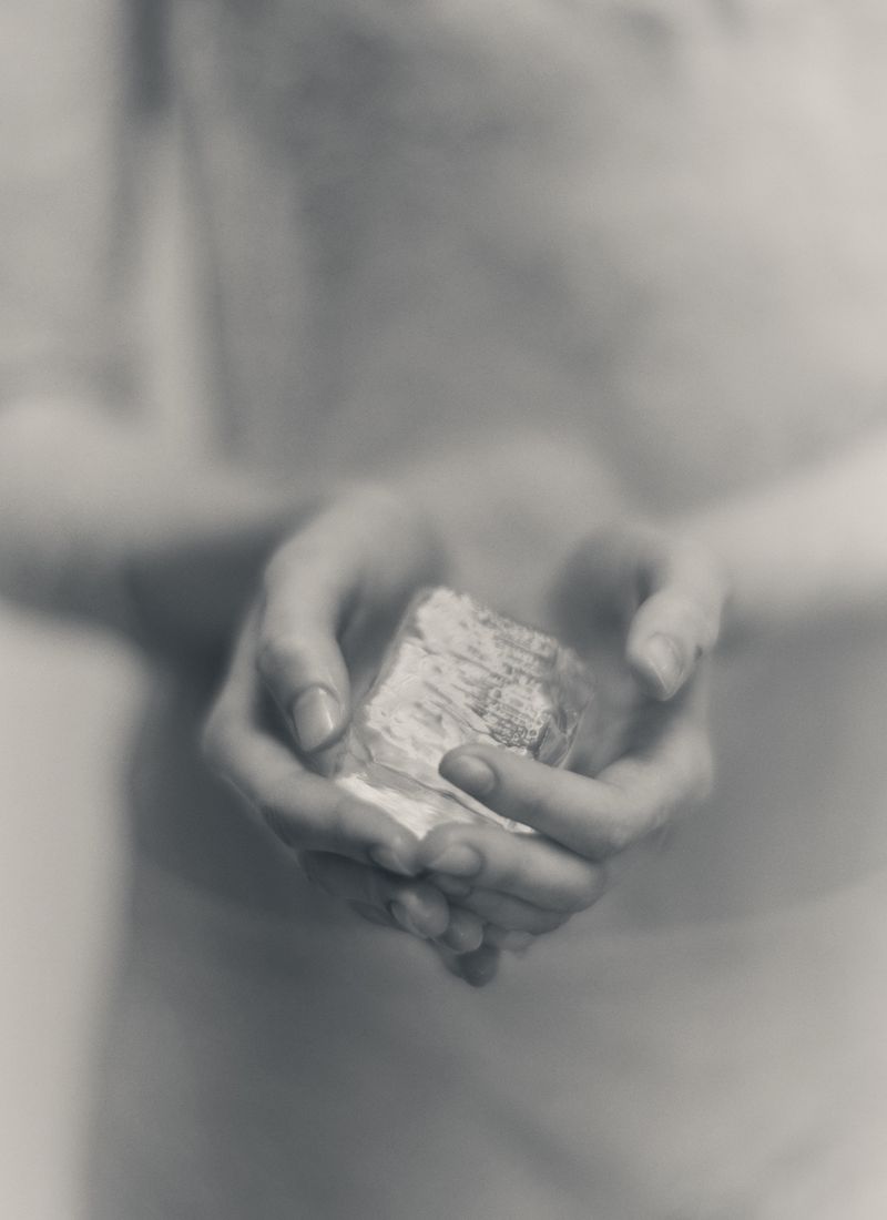 Close-up shot of an individual's hands cradling a rectangular object, set against a blurred background with monochrome tones, grayscale.