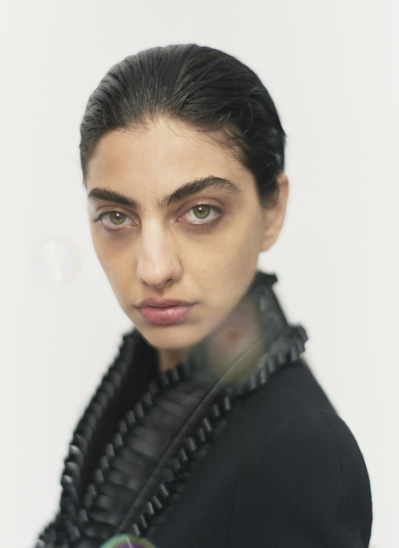 Portrait of a brunette woman in a black jacket with ruffled trim on a white background in a studio. Head and shoulders shot.