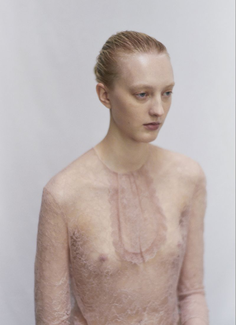 Young woman with blonde hair in a lace top poses in front of a white background in a studio headshot, fashion portrait photography.