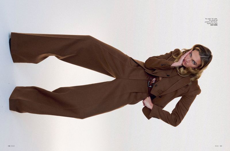 Fashion editorial shot of a blonde adult woman wearing a brown suit and posing against a white backdrop.