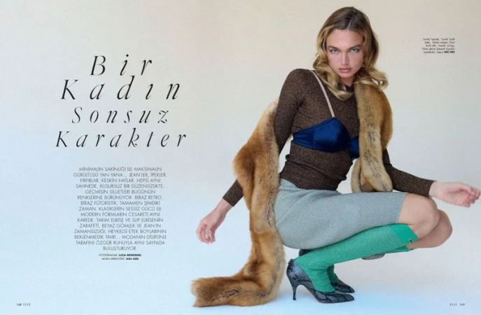 Fashion editorial shot of woman in brown top, blue bra, green socks and fur stole crouching in front of white backdrop.  
