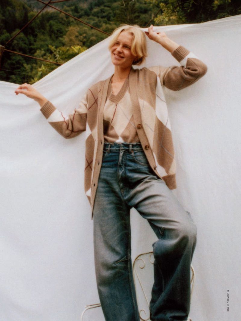 Model Steffi Cook poses in an argyle cardigan and wide-leg denim jeans in front of a draped white fabric backdrop outdoors.
