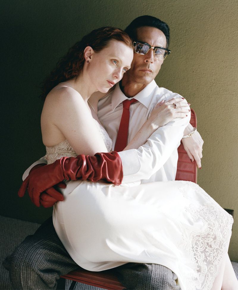 A stylish portrait showcases an adult couple in a studio setting, featuring a woman in a white dress and a man in a shirt and tie.