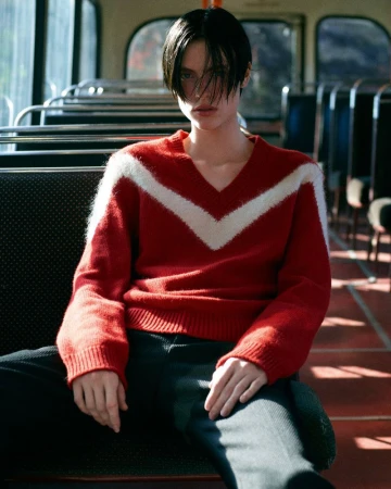 A young adult poses on a bus in a red and white sweater, with dark hair framing their face, creating a portrait-style image with a vintage feel.