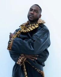 Skepta wearing a black leather jacket with animal print collar against a white background for Fantastic Man