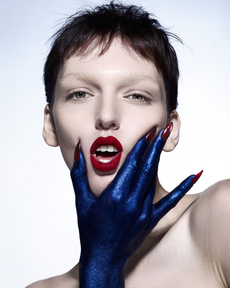 Close-up beauty shot of a fair-skinned woman with red lips, hand painted blue with red nails, and a light background. Beauty and fashion.