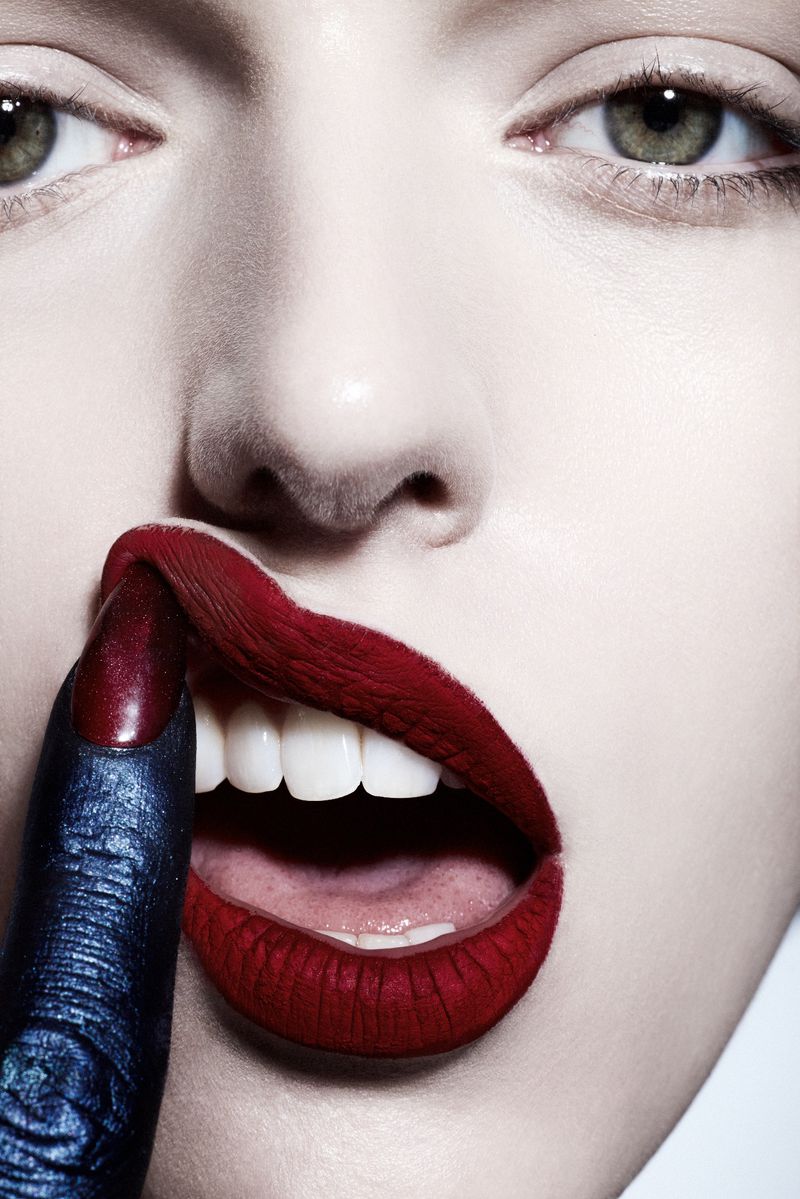Close-up of a woman's face with vibrant red lips, finger touching her mouth, pale skin and eyes, studio lighting, beauty and fashion concept.