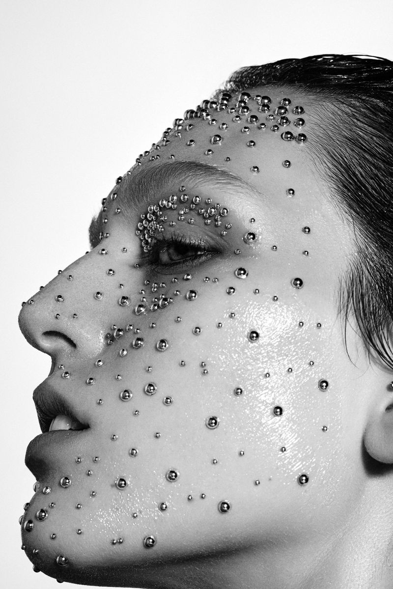 Monochrome portrait of a woman's face in profile, adorned with small silver spheres, capturing a modern beauty and skincare aesthetic.