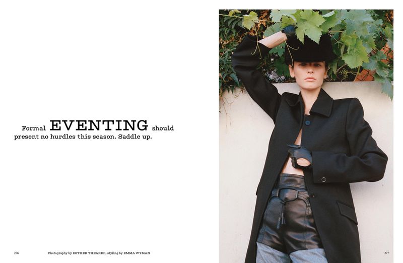 A fashion editorial shot featuring a female model in a black coat and hat, posing outdoors against a vine-covered wall on a sunny day.