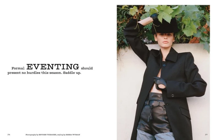 A fashion editorial shot featuring a female model in a black coat and hat, posing outdoors against a vine-covered wall on a sunny day.