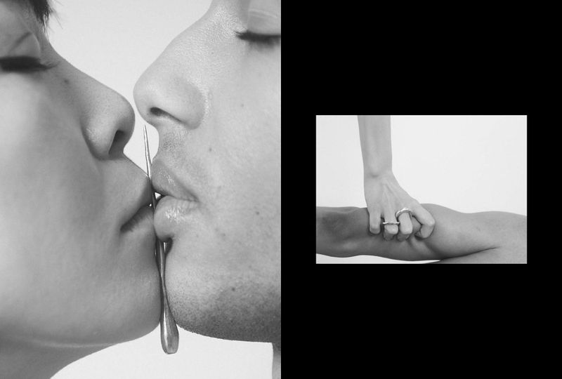 Monochrome image of a couple face to face with a metal object between their lips and a hand squeezing a leg with a ring on the finger.