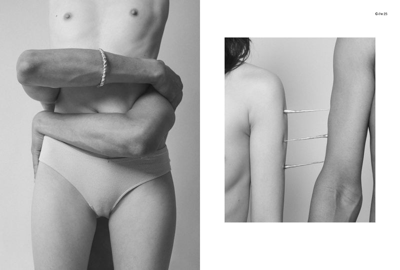 Two nude figures embrace in a monochrome image, their arms intertwined, against a plain background, showcasing a minimalist aesthetic.