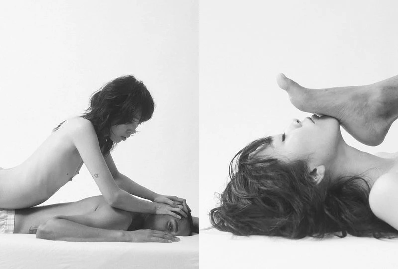 Monochrome portrait of a woman lying with a foot on her face; another woman lies on a man, hands on his head, in a white studio.
