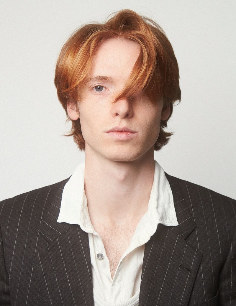 Portrait of a red-haired man in a pinstripe suit and white shirt. Close-up, studio lighting, fashion editorial style.