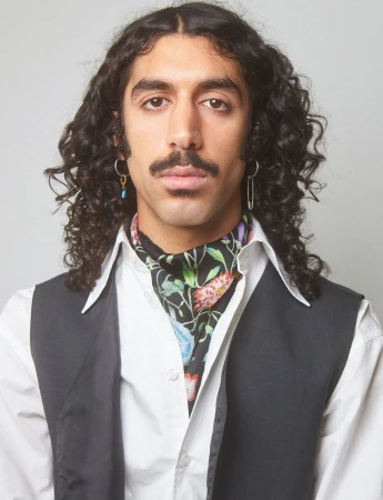 Portrait of a dark-haired adult male with a mustache wearing a floral ascot, black vest, and white shirt against a white background.