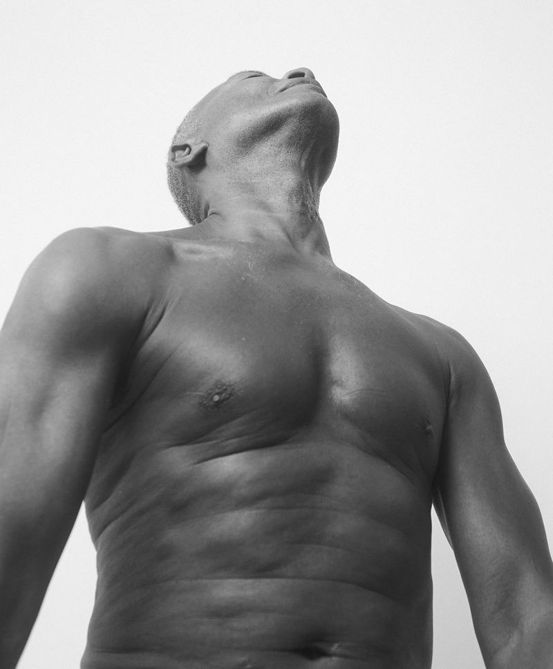 Black and white studio shot of a muscular, bald adult male with his head tilted back, torso bare against a plain background.